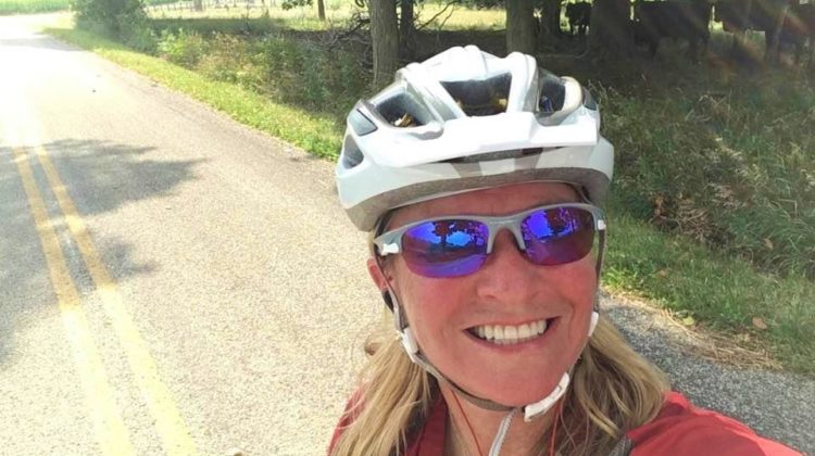 Leslie with a big smile, sunglasses and bike helmet.